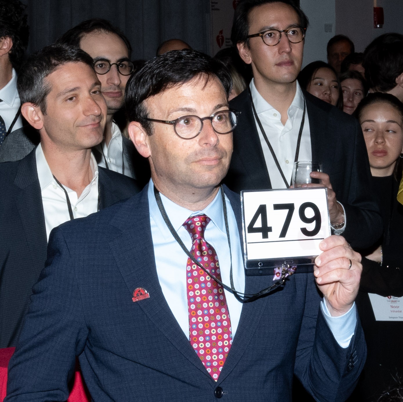 Man wearing Cor Vitae member pin holding up bidder number 479.